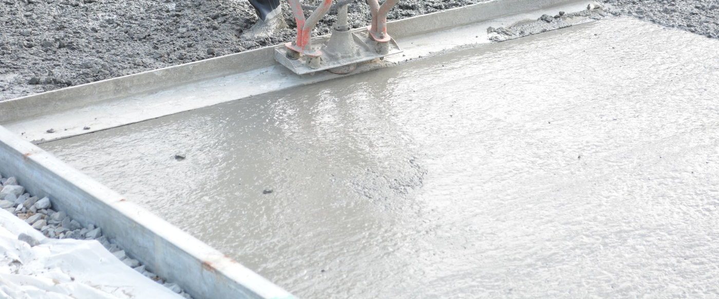Licensed stock photograph: a freshly poured concrete slab being levelled inside its forms with a power screed.